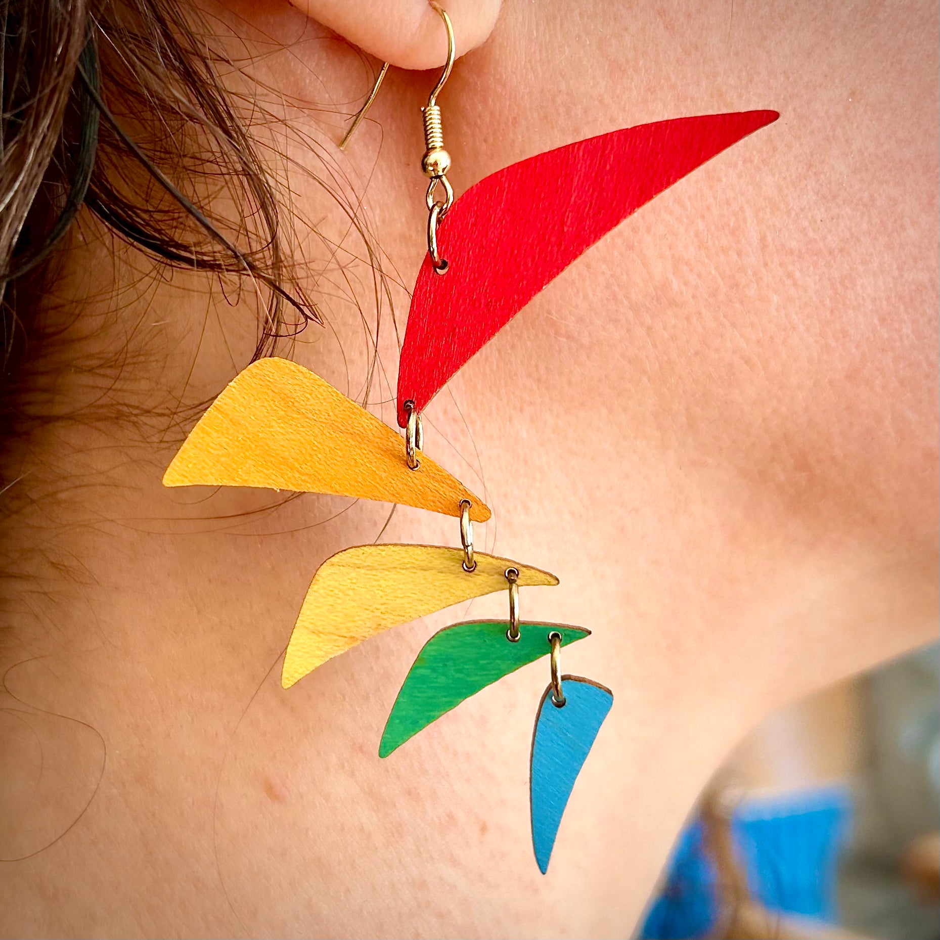 Colorful feather-shaped earrings worn by a person.
