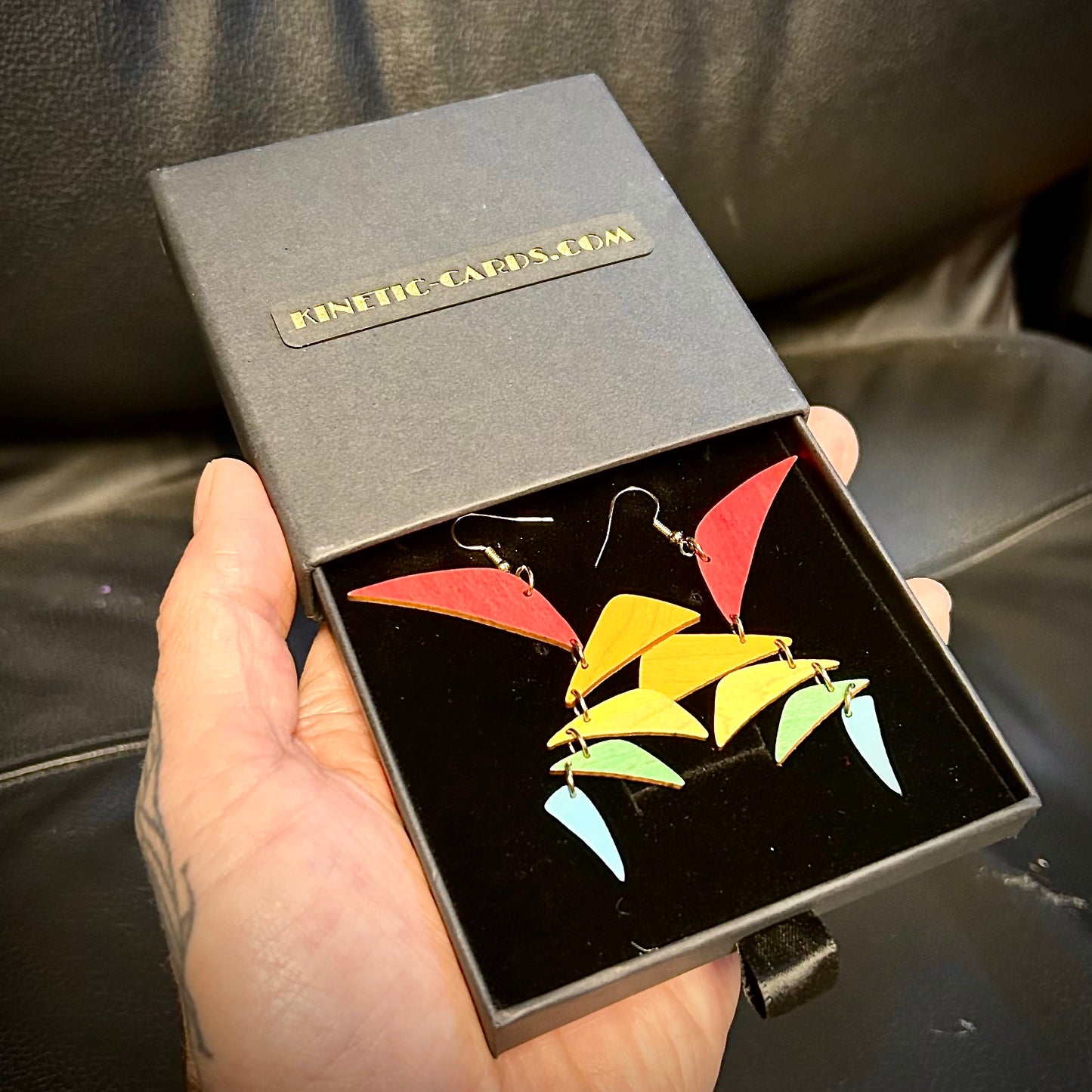Colorful earrings in a black box held by a hand on a dark surface