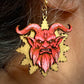 Earring with red demon face design on a gold background worn by a person.
