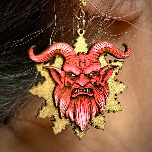 Earring with red demon face design on a gold background worn by a person.