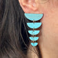 Close-up of a person wearing a turquoise earring with multiple layered half-circle shapes.