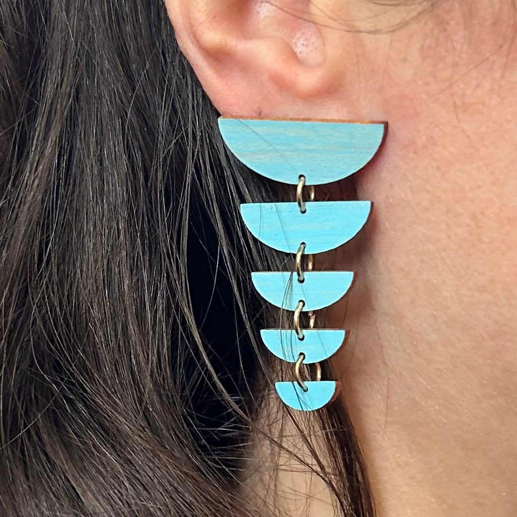 Close-up of a person wearing a turquoise earring with multiple layered half-circle shapes.