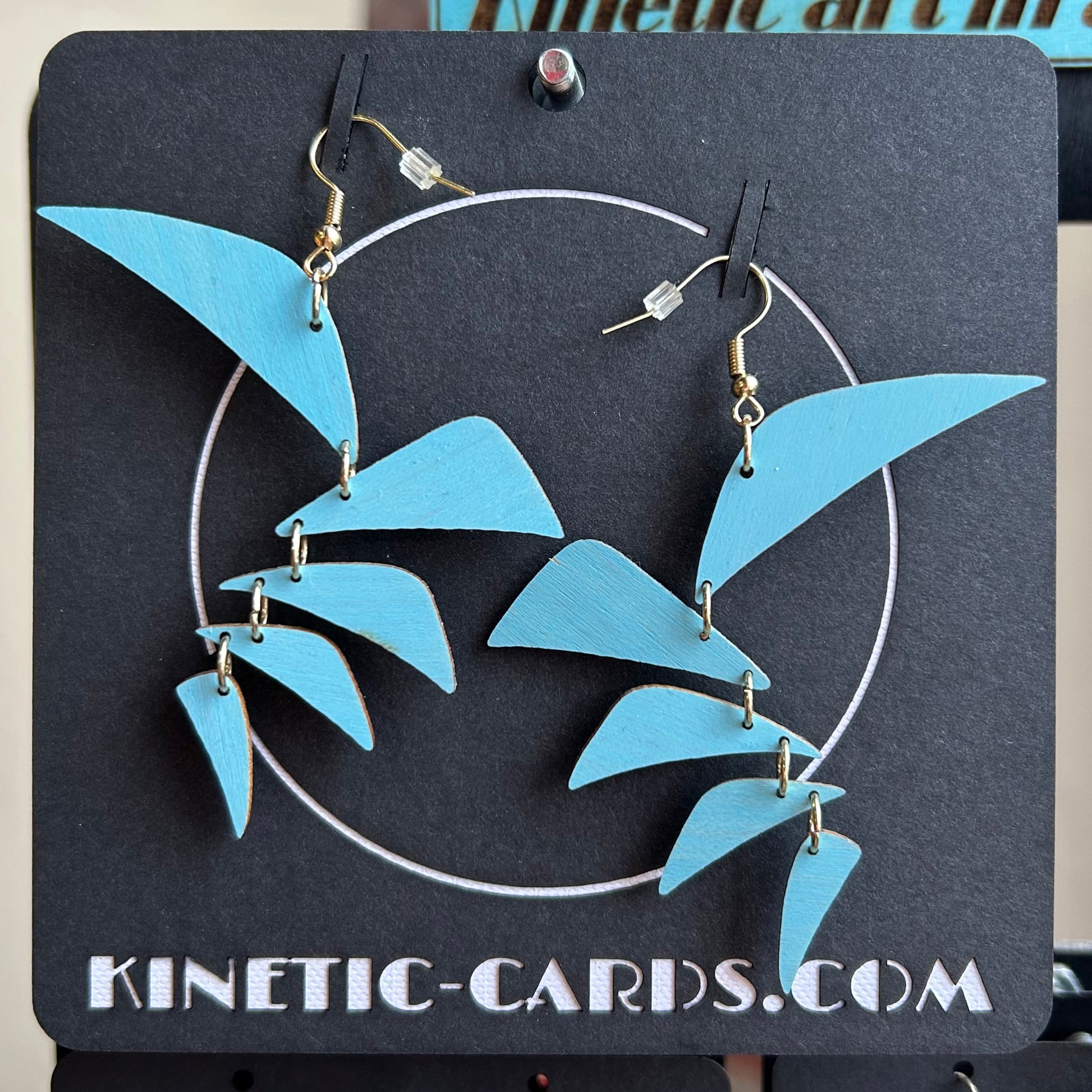 Blue leaf-shaped earrings on a black card with 'Kinetic-Cards.com' branding.