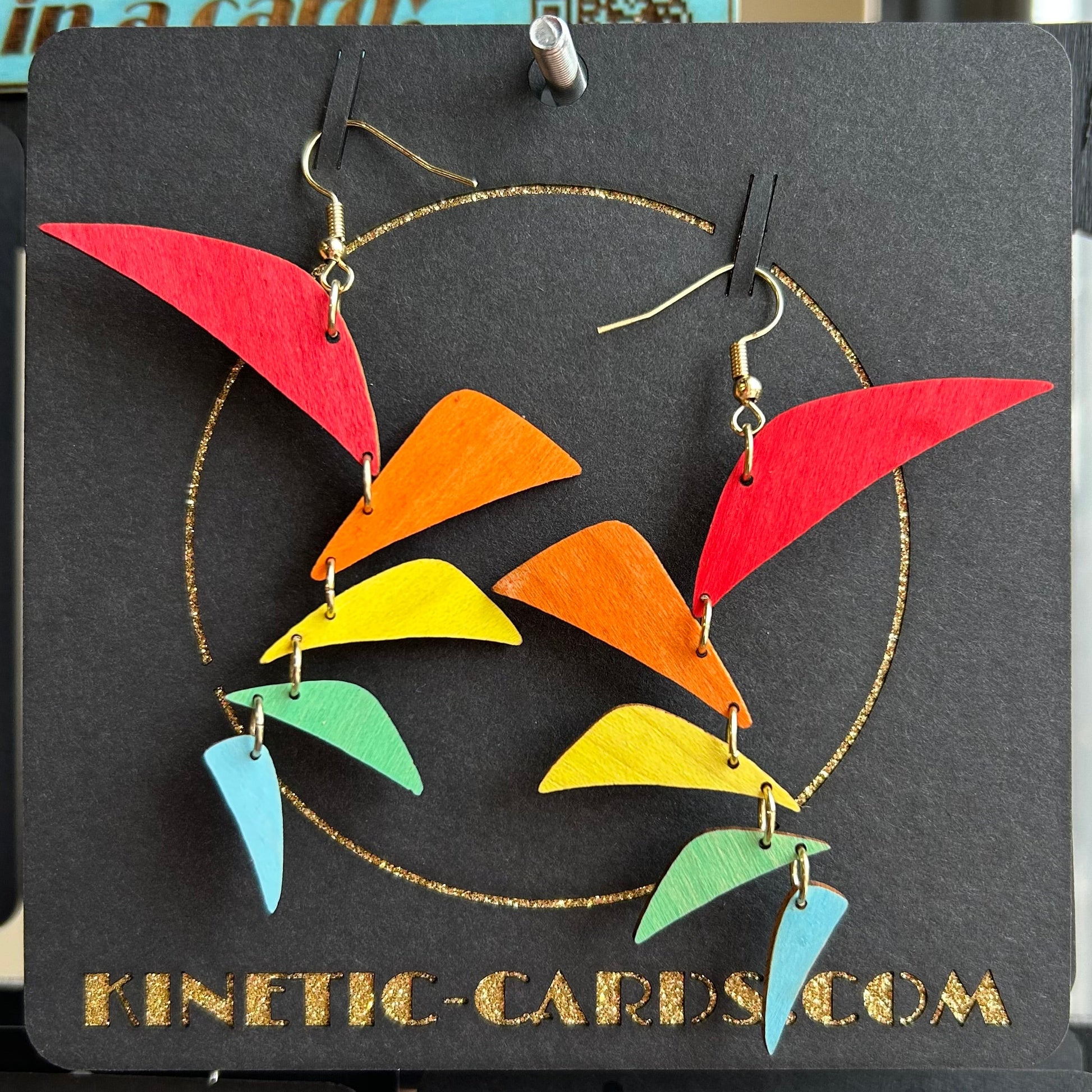 Colorful earrings on a Kinetic Cards display card with a blurred background.