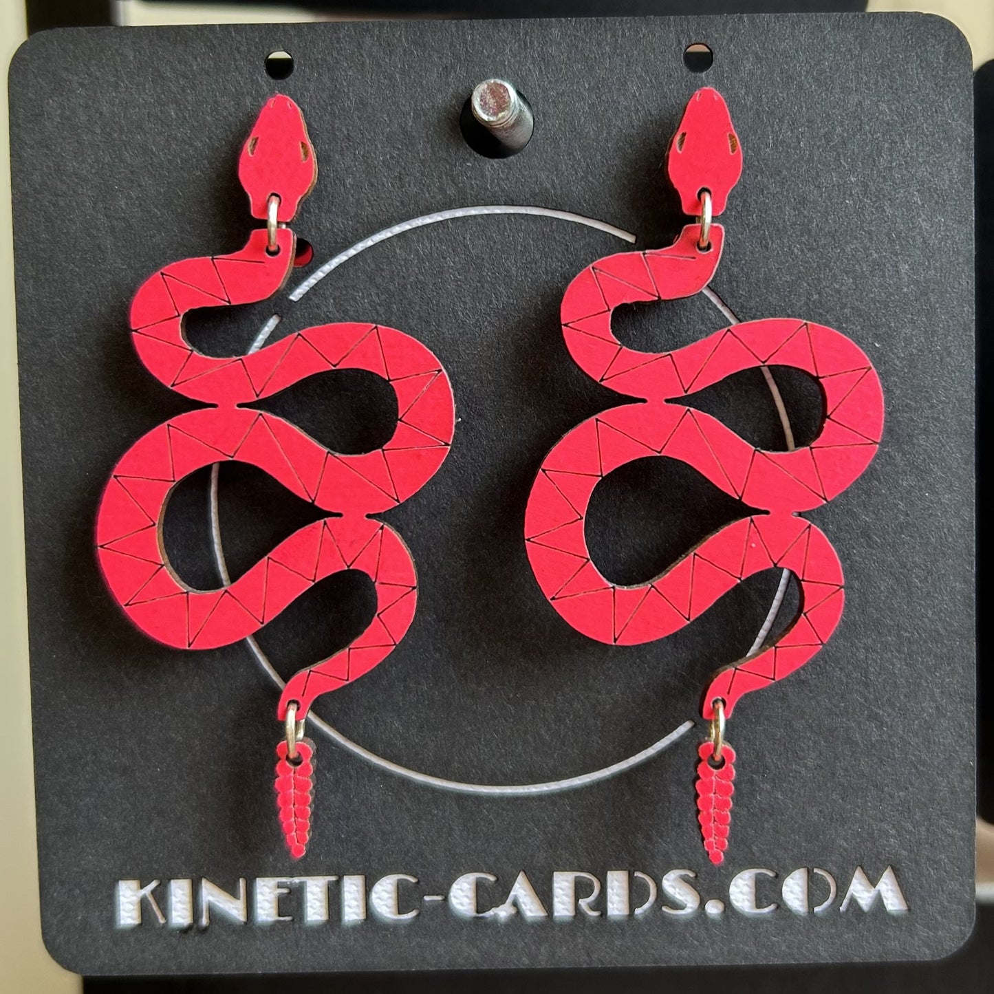 Red snake-shaped earrings on a black card with 'Kinetic-Cards.com' branding.