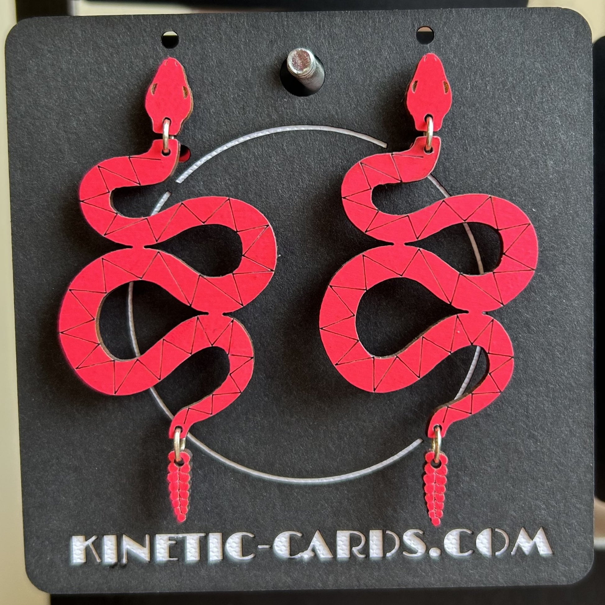 Red snake-shaped earrings on a black card with 'Kinetic-Cards.com' branding.