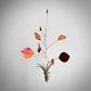 A hanging metal leaf wind spinner with copper-colored leaves, a dark burgundy leaf, and a small potted air plant at the center, suspended against a plain light gray background.