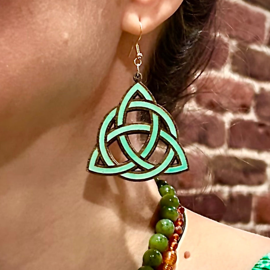 Green Celtic knot earring worn by a person with a brick wall background
