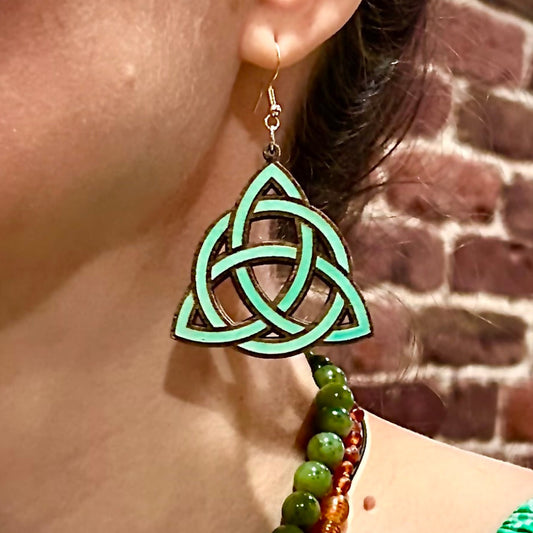 Green Celtic knot earring worn by a person with a brick wall background